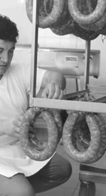 L'artigiano norcino di Sapori Mediterranei a Cirigliano mentre lavora e taglia manualmente i tagli scelti di carne suina sul banco per la produzione dei salumi tradizionali.